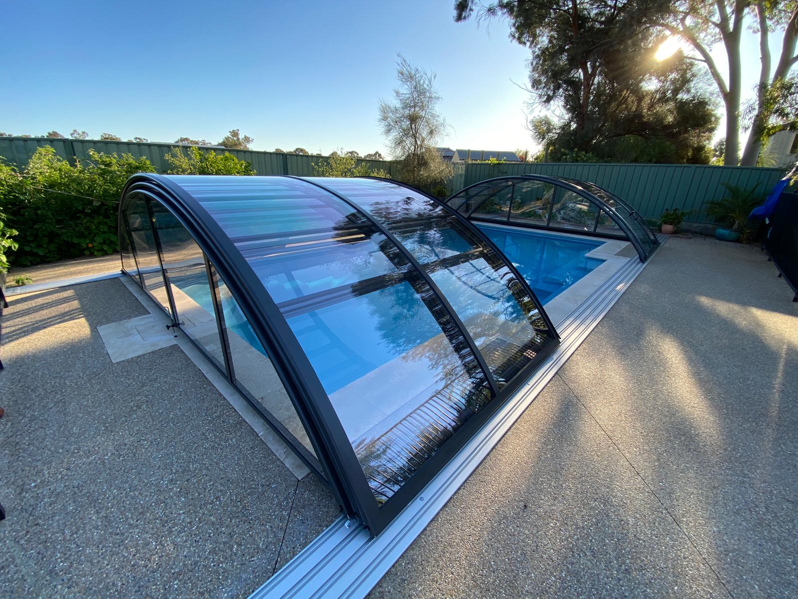 A large swimming pool with a telescopic pool enclosure opened in the middle in a melbourne garden at sunset